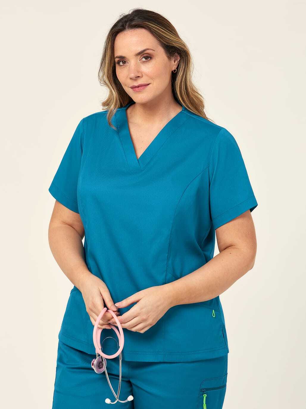 A woman in blue scrubs holding a pink stethoscope.
